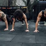 Three individuals performing push-ups together in a Mexico City gym setting.