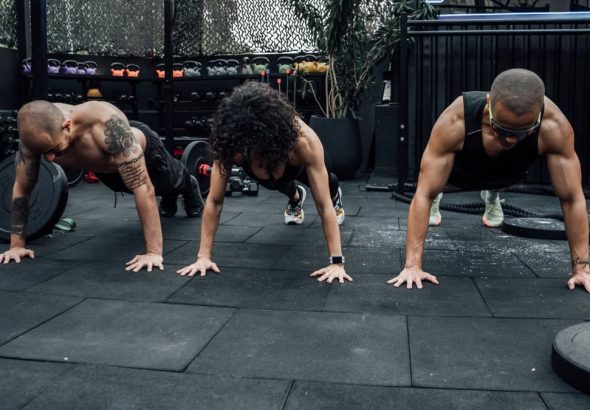 Three individuals performing push-ups together in a Mexico City gym setting.